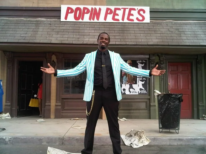 Popin Pete stands with open arms in front of a film set bearing his name.