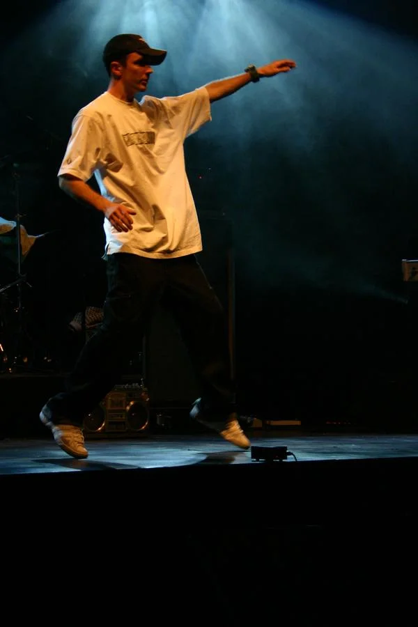 Stefan Bootin extends one arm on stage with his heels raised.